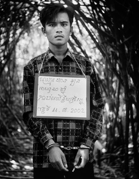A handcuffed poacher is photographed with a board bearing details of his name, age, plus the nature and date of his crime. Cambodia, 2002.
