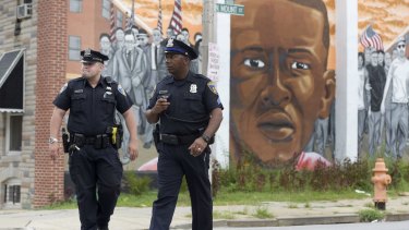 Baltimore police walk past a mural depicting Freddie Gray after prosecutors dropped remaining charges against the three officers still awaiting trial.