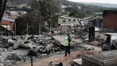 A police officer takes photos of the aftermath of the Tathra bushfires, which destroyed 68 homes.