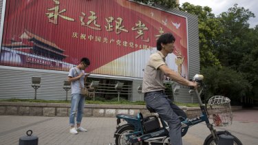 A man smokes near a billboard with the words 'Always follow the Communist Party' to mark the 94 anniversary of the founding of the Communist Party of China in Beijing.