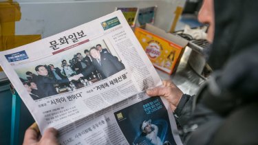 A man looks at a newspaper featuring a photograph of the meeting.