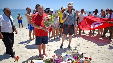 Tourists carry a Tunisian flag along Marhaba beach where 38 people were killed on Friday.