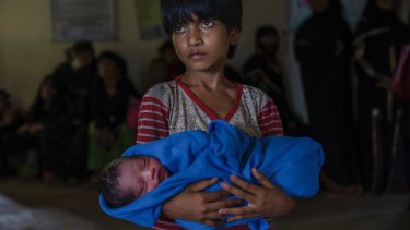 Rohingya Muslim girl Afeefa Bebi, who recently crossed over from Myanmar into Bangladesh, holds her few-hours-old brother as doctors check her mother Yasmeen Ara at a community hospital in Kutupalong refugee camp, Bangladesh on Wednesday.