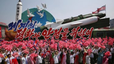 North Koreans wave as they march next to a float display of models of different missiles during a military parade in Pyongyang earlier this month.