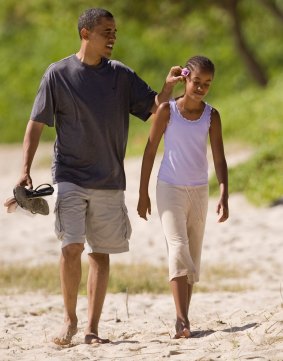 Then presidential candidate Senator Barack Obama adjusts a flower behind the ear of his daughter Malia, 10, as they walk on Kailua Beach in Hawaii.