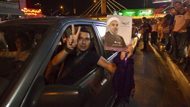 A man holds a picture of Iran's President Hassan Rouhani as he celebrates the nuclear deal with others in the streets.