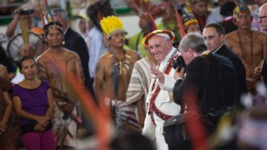 Wearing an indigenous headdress and jewelry, Pope Francis waves during a meeting with indigenous groups.