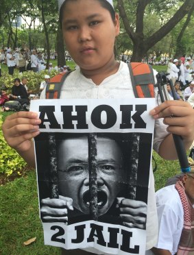 A young protester holds a poster demanding the imprisonment of Jakarta's governor, popularly known as Ahok.