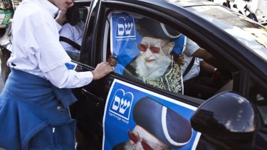 A supporter of the ultra-Orthodox Shas party holds a campaign poster depicting the party's spiritual leader, the late Rabbi Ovadia Yosef, in Bnei Brak near Tel Aviv.