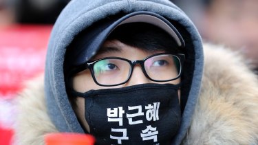 A protester wearing a mask, attends during a rally calling for impeachment of President Park Geun-hye. The letters read "Arrest Park Geun-hye." 