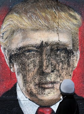 A woman passes by graffiti depicting US President-elect Donald Trump vandalized with paint, in Belgrade, Serbia.