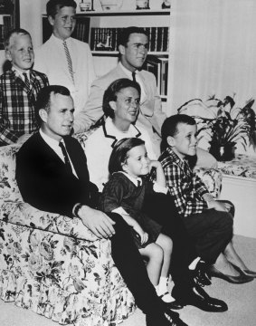 George H.W. Bush sits on the couch with his wife Barbara in 1964. George W. sits on the couch leg by his mother and Jeb is behind her.