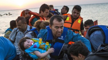 A man carries a girl in his arm as they arrive with other migrants just after dawn on a dinghy after crossing from Turkey to the island of Kos in southeastern Greece.