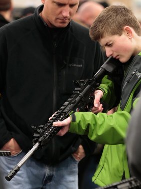 A boy holds a semi-automatic assault rifle for sale while his father watches at a Utah gun show.