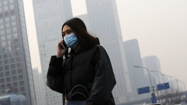 A woman wearing a mask to protect herself from pollutants walks past office buildings shrouded in haze in Beijing.
