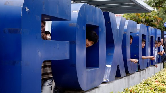 Employees at Hon Hai's Foxconn plant peek out from the back of a company sign in Shenzhen, China.