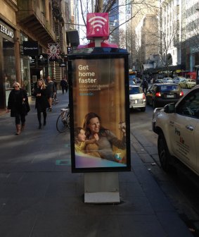 A Telstra telephone booth in Melbourne's Collins Street with an advertising display sign tacked on the side.