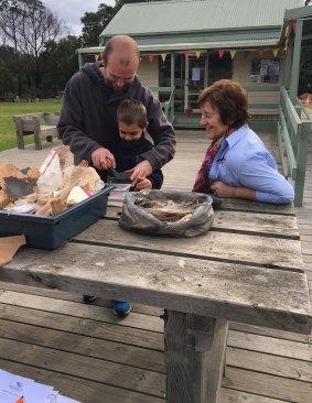 Trent Johns and son Tyrese mixing ochre to decorate tables for a Naidoc week dinner. MCH nurse Chris Fyson, who introduced the father and son to the Koori Kids Bush Playgroup, looks on.