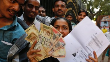 An woman shows discontinued Indian currency notes and a photocopied ID card as she queues outside a bank. Modi's experiment has upset many.