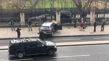 People stand near a crashed car and an injured person lying on the ground, right, on Bridge Street near the Houses of Parliament in London on Wednesday.