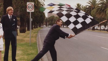 Former premier Jeff Kennett waves a chequered flag in Albert Park with Ron Walker looking on 