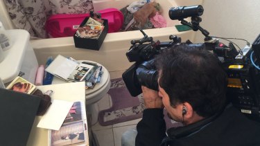 A cameraman films photo albums scattered on top of the toilet in the apartment.