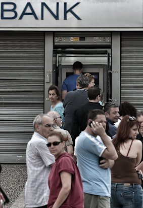 People stand in a queue to use ATM machines to withdraw cash at a bank in Athens.