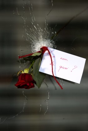 A rose placed in a bullet hole with a card stating "In the name of what" in Paris.