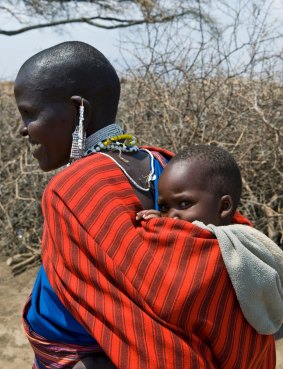 A local woman with a little child carried in traditional way walks through Ngorongoro Park, Tanzania.