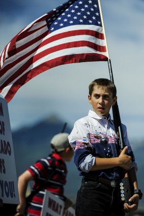 A 12-year-old carries a US flag in the barrel of his shotgun at a gun rights rally in Colorado. US culture inclines towards reverence, writes Martin Flanagan.