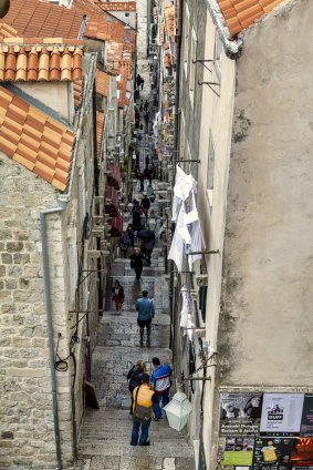 Tourists walk on a typical alley in Dubrovnik, Croatia. Dubrovnik is one of the oldest towns at the Adriatic Sea, and it is a popular destination for tourists and cruisers. 