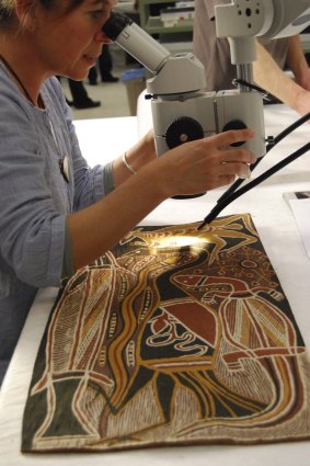 Conservator Chloe Bussenschutt works on a bark painting by David Malangi, Totemic Animals.