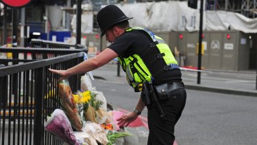 A police officer lays flowers passed to him by members of the public on the north side of London Bridge.