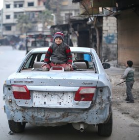 A child plays on top of a car damaged by an explosion in Eastern Ghouta.