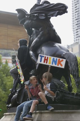 Children observe the rally from on a statue at the State Library.