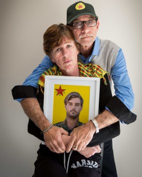 Michele and Keith Harding, wearing a YPG scarf  and cap, hold a portrait of their son Reece.