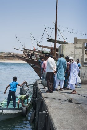 Bangladeshi fishermen landing some shark at dock in Mirbat, while an elderly local looks on.