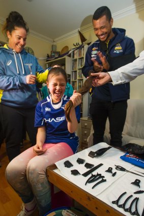 Lizzy Marshall,11, gets her head shaved by Wallaroos' Louise Burrows and Brumbies' Aidan Toua. 