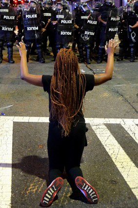 A protester places raises her arms while on her knees in front of officers in riot gear in Charlotte on Wednesday.