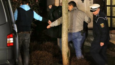 A person covered with a black blanket is led by police officers from the Lubitz family house in Montabaur on Thursday.