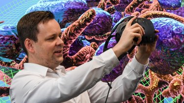UNSW's John McGhee holds the virtual reality mask that allows you to explore inside a breast cancer cell. Mitochondria and endosomes form the backdrop.