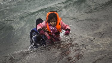 A man and his child - both wearing real life vests - struggle to shore after arriving at the Greek island of Lesbos. 
