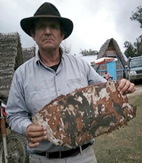 Blaine Gibson holding a piece of aircraft debris on a beach in Madagascar.