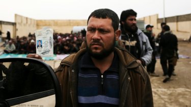 Fleeing: A man holds up his identification card to an Iraqi intelligence officer screening men and boys escaping Mosul.