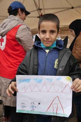 A refugee child displays his drawing.