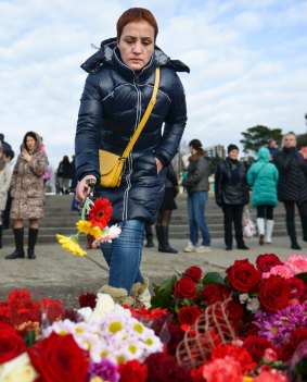 A woman lays flowers at a makeshift memorial at a pier in Sochi, Russia.