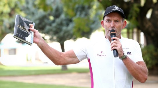 Former prime minister Tony Abbott holds up a copy of his book <i>Battlelines</i> in Forbes during the 2016 Pollie Pedal tour.