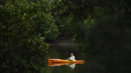 A man fishing from his small boat on the Cooks River at Kendrick Park in Tempe, Sydney.