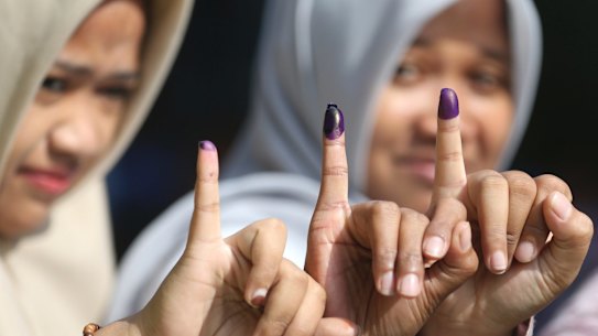 Women show their ink-stained fingers after voting during the runoff election in Jakarta.