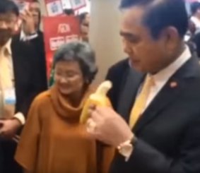 The Thai Prime Minister tries a banana at an exhibition.
